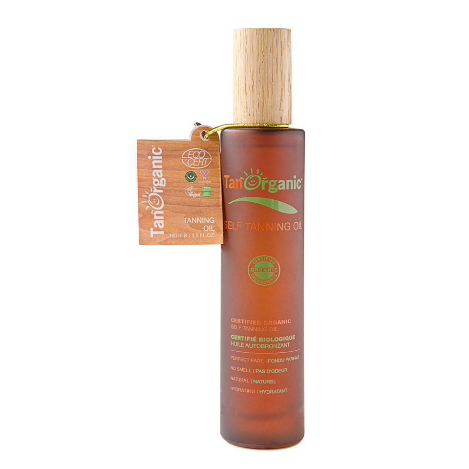 Transparent brown bottle with a wooden cap, labeled "TanOrganic Self Tanning Oil," featuring a citrus scent, 100 ml, and a tag indicating organic certification.