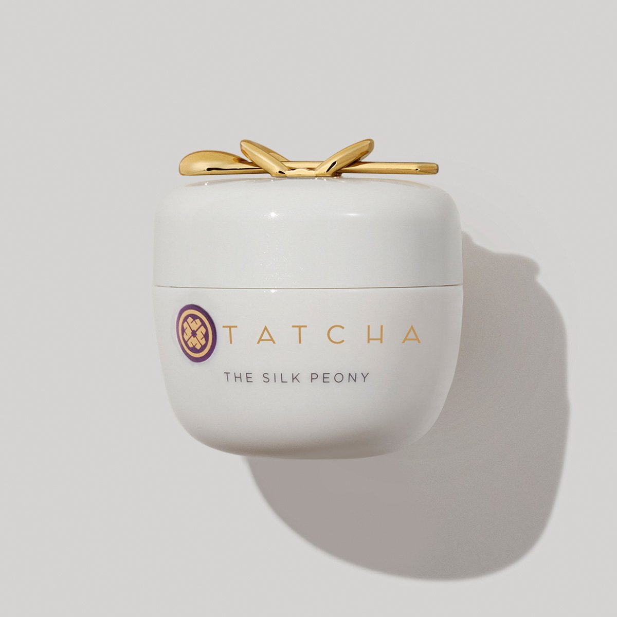 White jar with a gold lid featuring a decorative bow, labeled "Tatcha The Silk Peony Smoothing Eye Cream," containing 15 ml of Japanese skincare product.