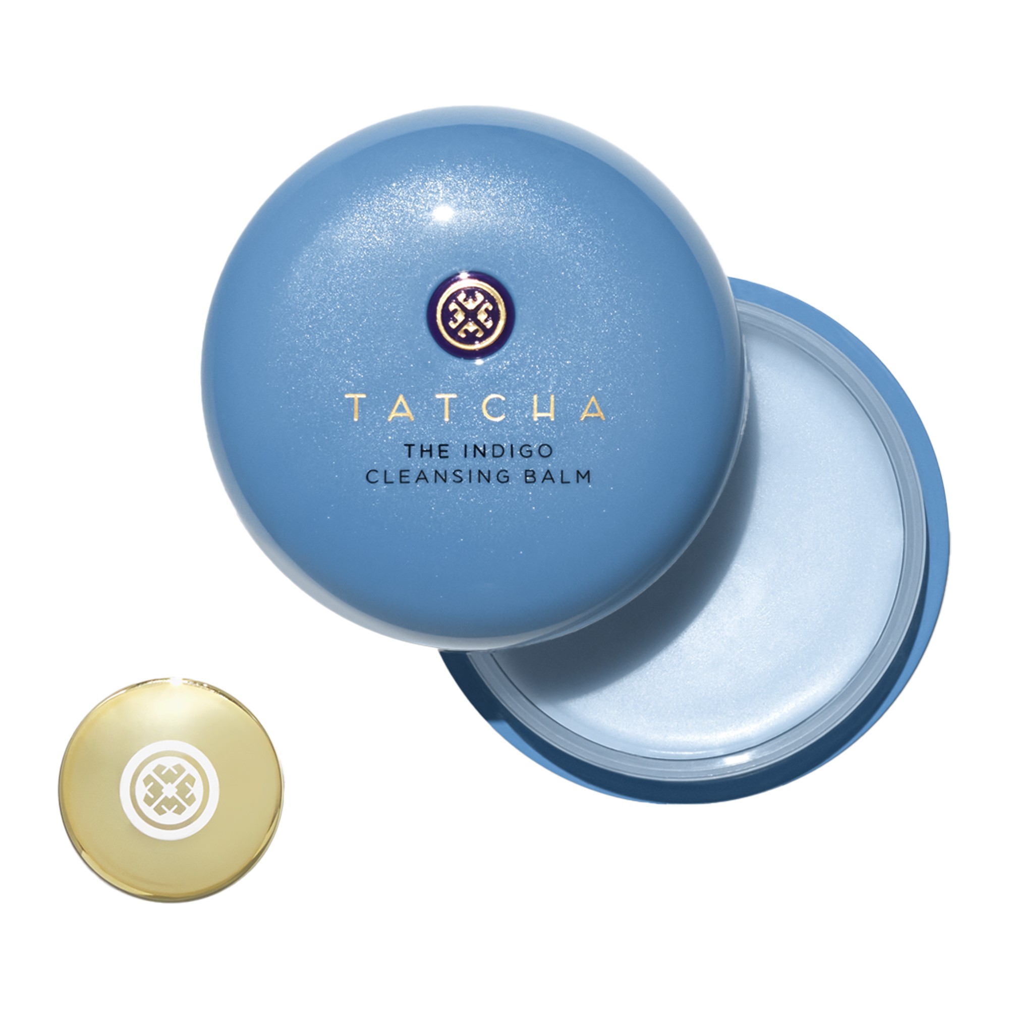 Round, light blue container with a gold emblem on top, revealing a soft, pale blue cleansing balm inside, labeled "Tatcha Indigo Cleansing Balm for Sensitive Skin."