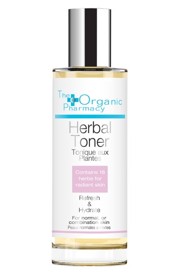 Clear glass bottle of The Organic Pharmacy Herbal Toner, featuring a white label with blue and pink accents, highlighting 18 herbs for radiant skin, suitable for normal or combination skin.