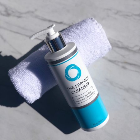 White pump bottle with a turquoise and silver design, labeled "THE PERFECT CLEANSER," alongside a white towel on a marble surface.