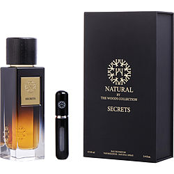 Clear glass bottle with a black wooden cap, featuring a gold label reading "Secrets," alongside a sleek black travel spray case, all in a black box with gold accents.