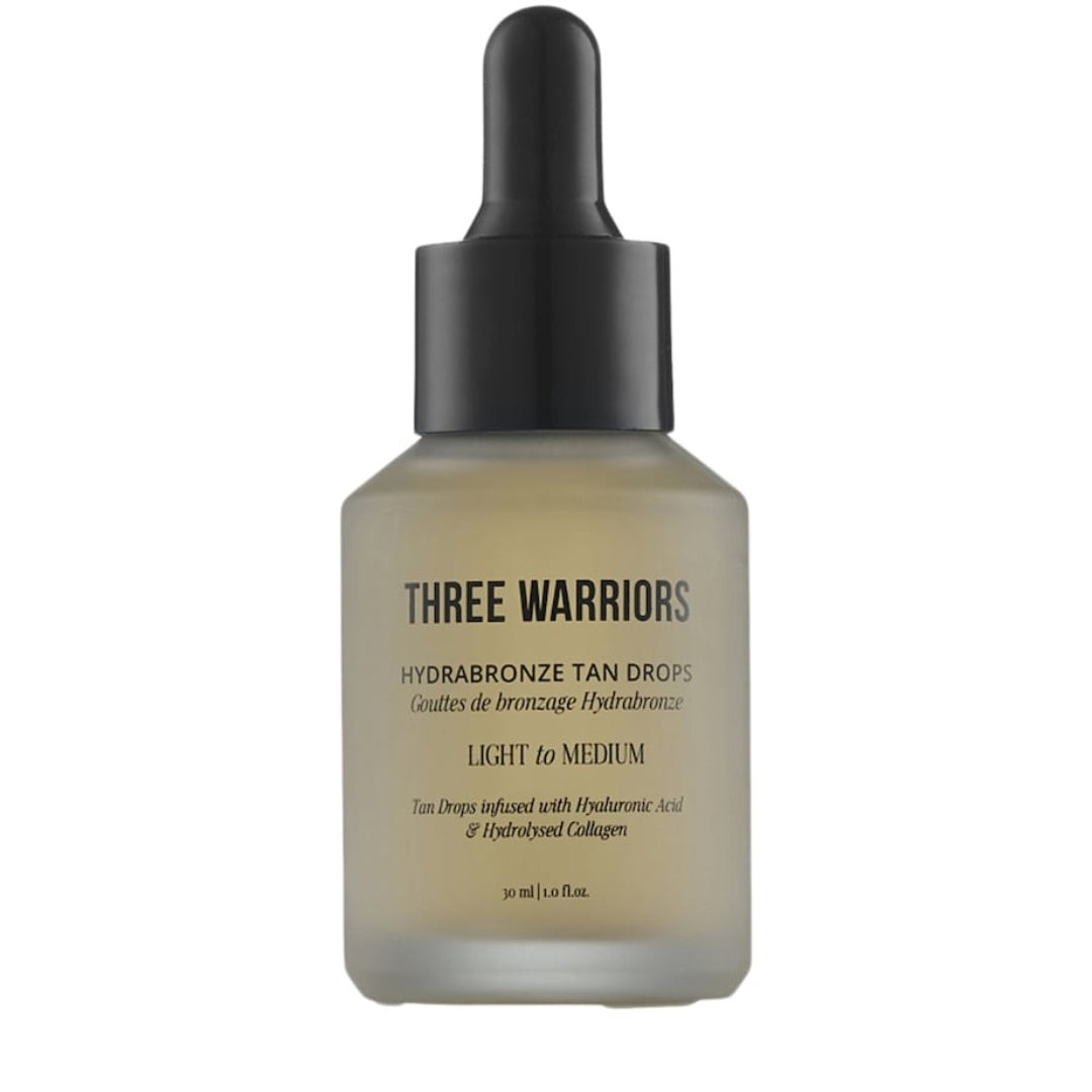 Clear glass bottle with a black dropper cap, labeled "Three Warriors Hydrabronze Tan Drops - Medium to Dark," featuring a frosted finish and gold lettering.