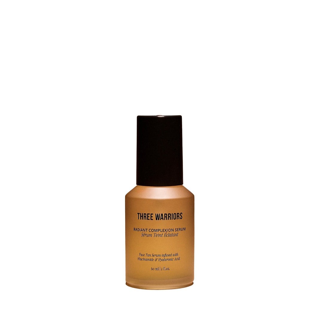 A frosted glass bottle with a matte black pump top, containing a golden serum labeled "Three Warriors Radiant Complexion Serum" by Sonia Kruger, 60ml.
