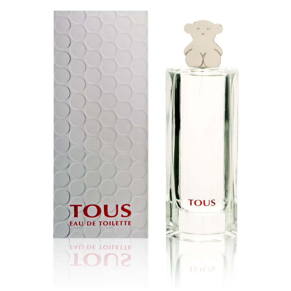 Clear glass bottle with a teddy bear-shaped cap, featuring a simple, elegant design; accompanied by a textured white box with a circular pattern and red "TOUS" branding.