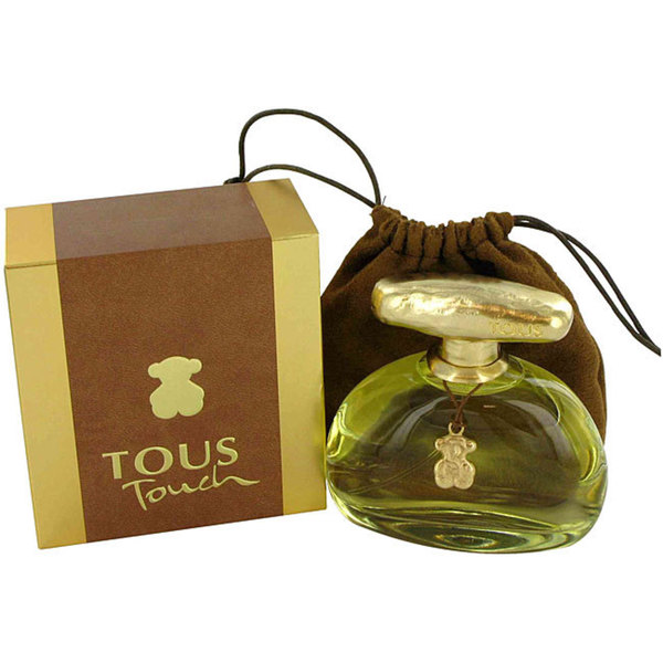 Clear glass bottle with a gold cap, featuring a teddy bear charm, alongside a brown box and a matching brown drawstring pouch, all labeled "Tous Touch."