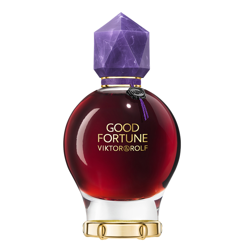 Round glass bottle with a deep red liquid, topped by a purple geometric cap and adorned with a gold band, featuring the label "GOOD FORTUNE VIKTOR&ROLF" in bold lettering.