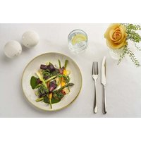 Plate with mixed greens and asparagus, lemon water, cutlery, salt and pepper shakers, and yellow rose in vase.
