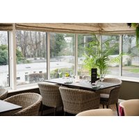 Dining area with wicker chairs, dark wood table, large windows, and greenery at Woodlands Hall Hotel, North Wales.