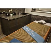 Massage table with patterned brown and blue linens in a spa room, featuring a dark wood counter and sink.