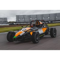 Orange and black Ariel Atom sports car on a racetrack, open-frame design with visible roll cage and driver.