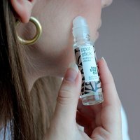 Clear roll-on bottle of Australian Bodycare Spot Stick with botanical pattern, applied to cheek.