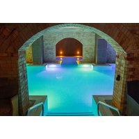 Indoor spa pool with glowing blue water, arched stone ceiling, and ambient lighting.