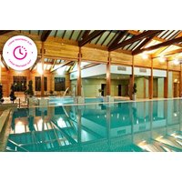 Indoor pool with wooden beams, lounge chairs, and a Bannatyne Spa logo on the wall.
