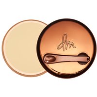 Round bronze compact with "dm" logo, containing beige blurring balm powder, by Danessa Myricks Beauty.