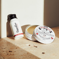 Dapper Dan Beard Oil 30ml in a white bottle with black cap, next to an open tin of beard balm on a stone surface.