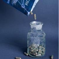 Blue Hifas da Terra supplement pack pouring capsules into a clear glass jar on a dark background.