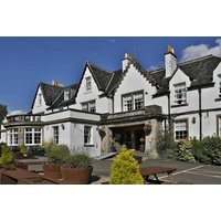 Buchanan Arms Hotel exterior, white facade, gabled roof, surrounded by greenery, clear sky above.