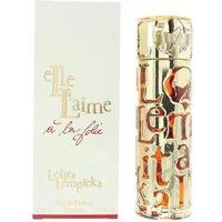 Gold cylindrical perfume bottle with embossed text, next to white box labeled "Elle L'aime A La Folie" by Lolita Lempicka.