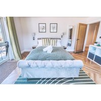 Luxurious spa stay room with plush bed, green throw, striped pillows, and modern decor, including framed wall art.