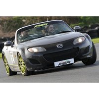 Black Mazda convertible sports car with green wheels on a racetrack, driver smiling, PSR Experience branding.