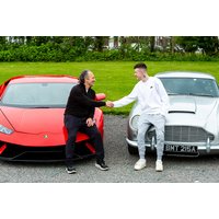 Red Lamborghini and silver classic car parked on gravel, two men shaking hands between them.