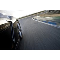 Black sports car on a racetrack, blurred motion, showcasing sleek design and speed, part of a driving experience package.