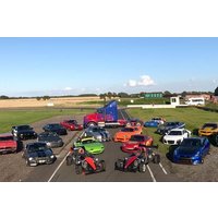 Various colorful supercars arranged on a racetrack with a blue truck in the background under a clear sky.