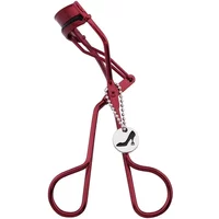 Red Tweezerman eyelash curler with shoe charm and ergonomic handles.