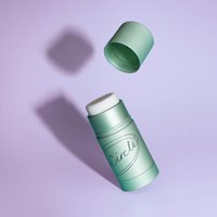 Green UpCircle refillable deodorant stick with macadamia and bergamot, open cap, on a light purple background.