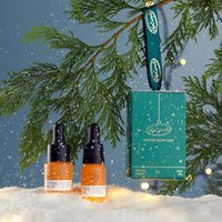 Green box with "Winter Glow Duo" text, two amber dropper bottles, snowy background, and pine branch.