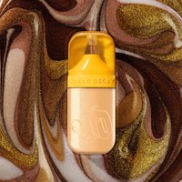 Gold Urban Decay Bond Highlighter with a sleek capsule design on a swirling brown and gold background.