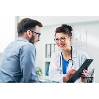 Doctor in white coat with stethoscope discussing health MOT with a man in a blue shirt, holding a clipboard.