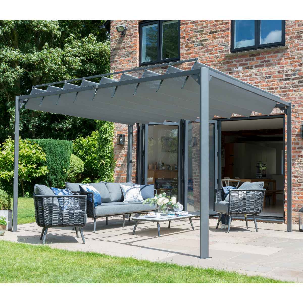 Adjustable 10' x 10' gray metal gazebo with a slatted roof, featuring a stylish outdoor seating area with gray cushions and wicker chairs on a stone patio.