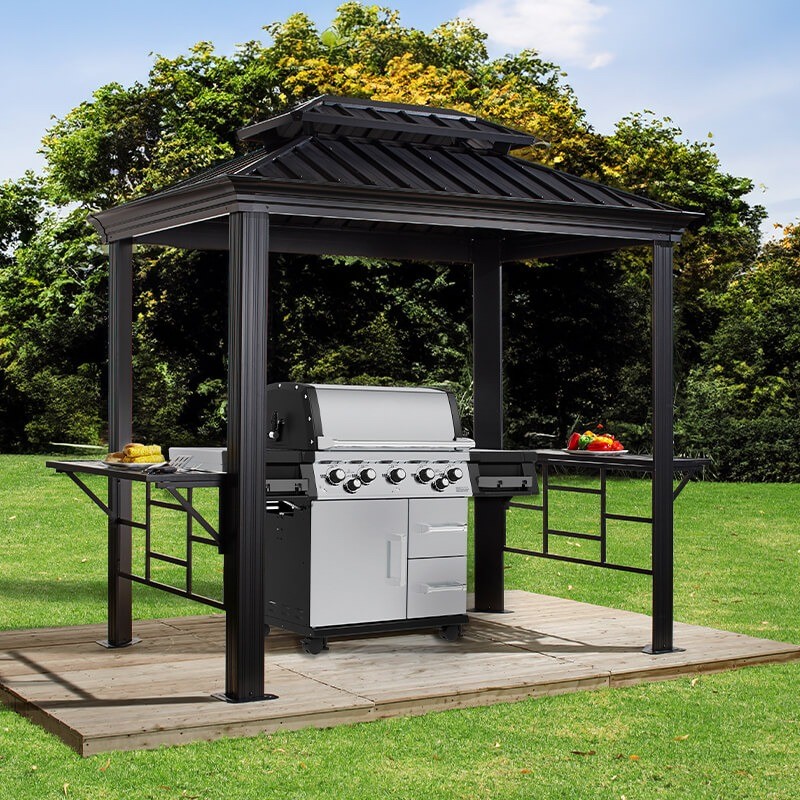 10' x 6' anthracite metal gazebo with a sloped roof, featuring a built-in stainless steel BBQ grill and side tables, set on a wooden deck in a green garden.