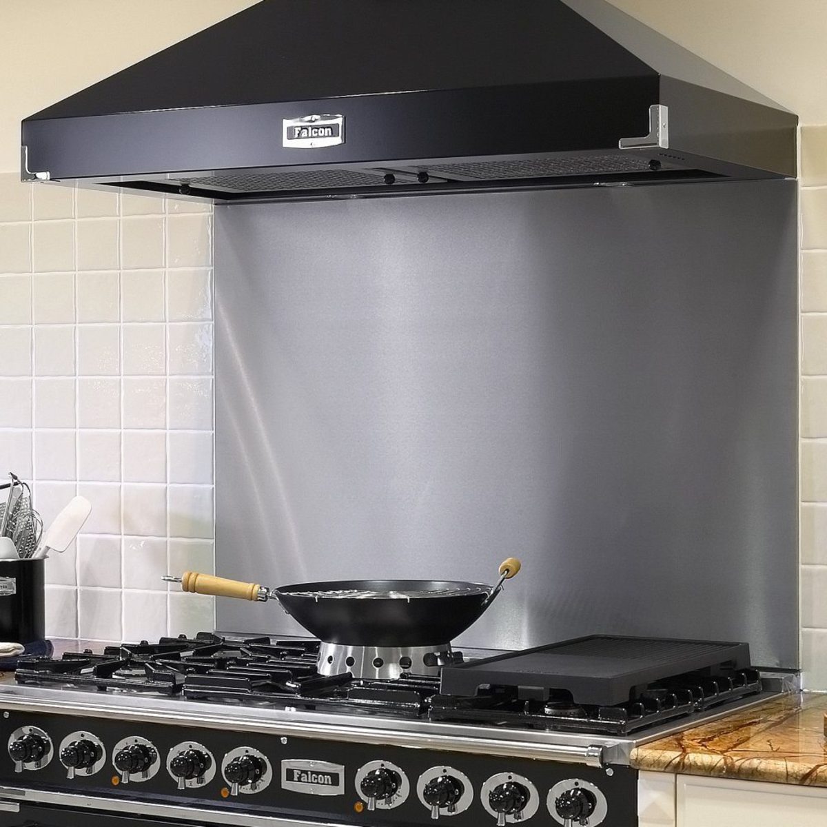 Stainless steel splashback measuring 1092mm, featuring a sleek, reflective surface, installed behind a black range hood and gas stove with a frying pan on the burner.