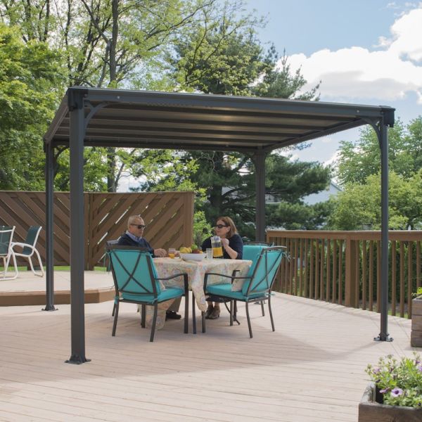 A 10'x10' Palram Canopia Milano 3000 garden gazebo with a dark gray metal frame and a slatted roof, providing shade over a table with two turquoise chairs on a wooden deck.