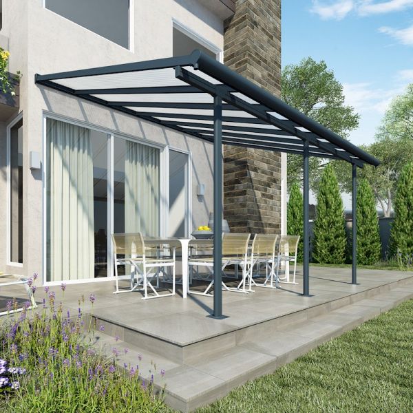 A grey Palram Canopia Sierra patio cover with a metal frame, featuring a sloped roof, providing shade over a dining set on a stone patio surrounded by greenery.