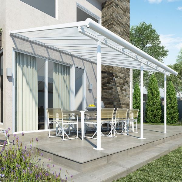 White aluminum patio cover with a sloped roof, supported by sturdy posts, extending over a dining area with a table and chairs, surrounded by greenery and stone walls.