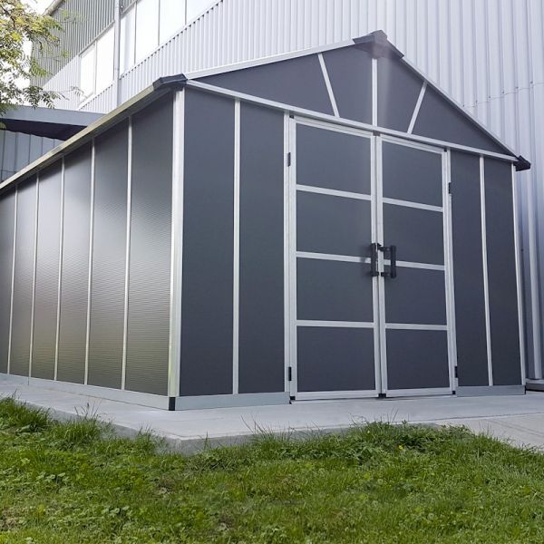 Dark grey plastic shed with a skylight, featuring a gabled roof, double doors, and a sturdy aluminum frame, set on a concrete base with grass surrounding it.