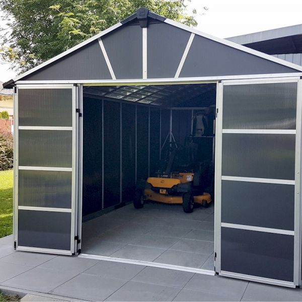 Dark grey plastic shed with a skylight, featuring double doors, a peaked roof, and a spacious interior, set on a paved area with a lawn in the background.