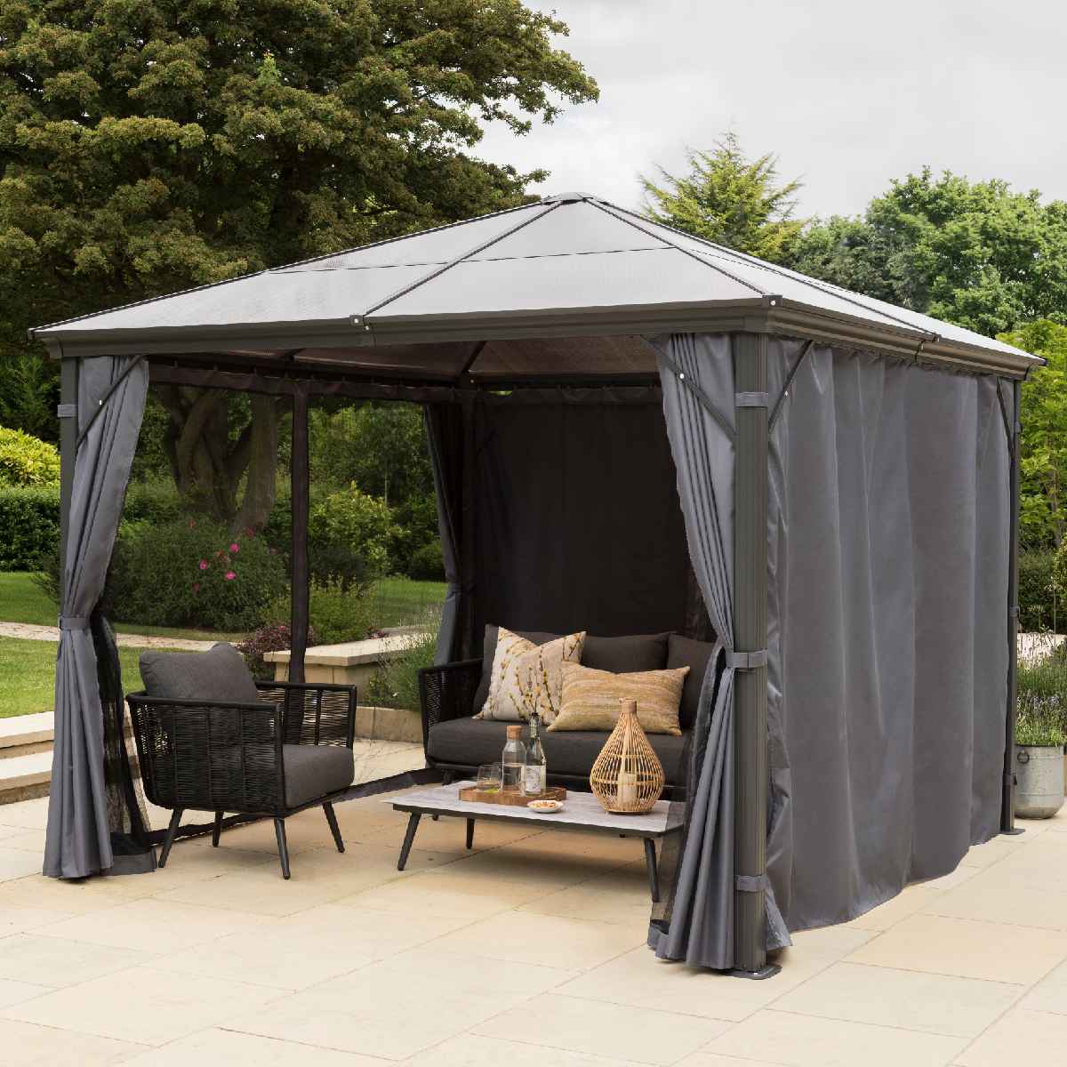 12' x 10' grey polycarbonate garden gazebo featuring a peaked roof, mesh side panels, and curtains, with a cozy seating area including a table and cushions.