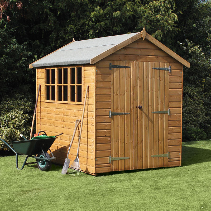 Traditional heavy-duty wooden garden shed in natural wood finish, featuring a sloped apex roof, double doors, and a window, surrounded by gardening tools on green grass.