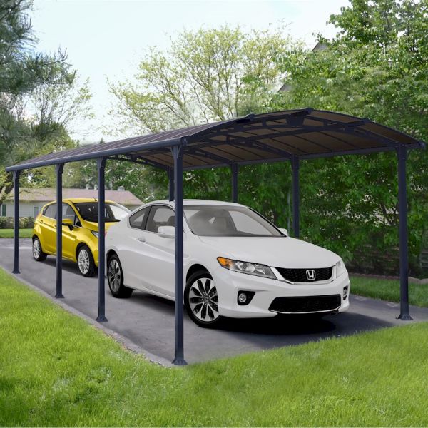 Grey metal carport with a curved roof, measuring 12' x 28', providing shelter for two cars, set against a green landscape with trees and grass.