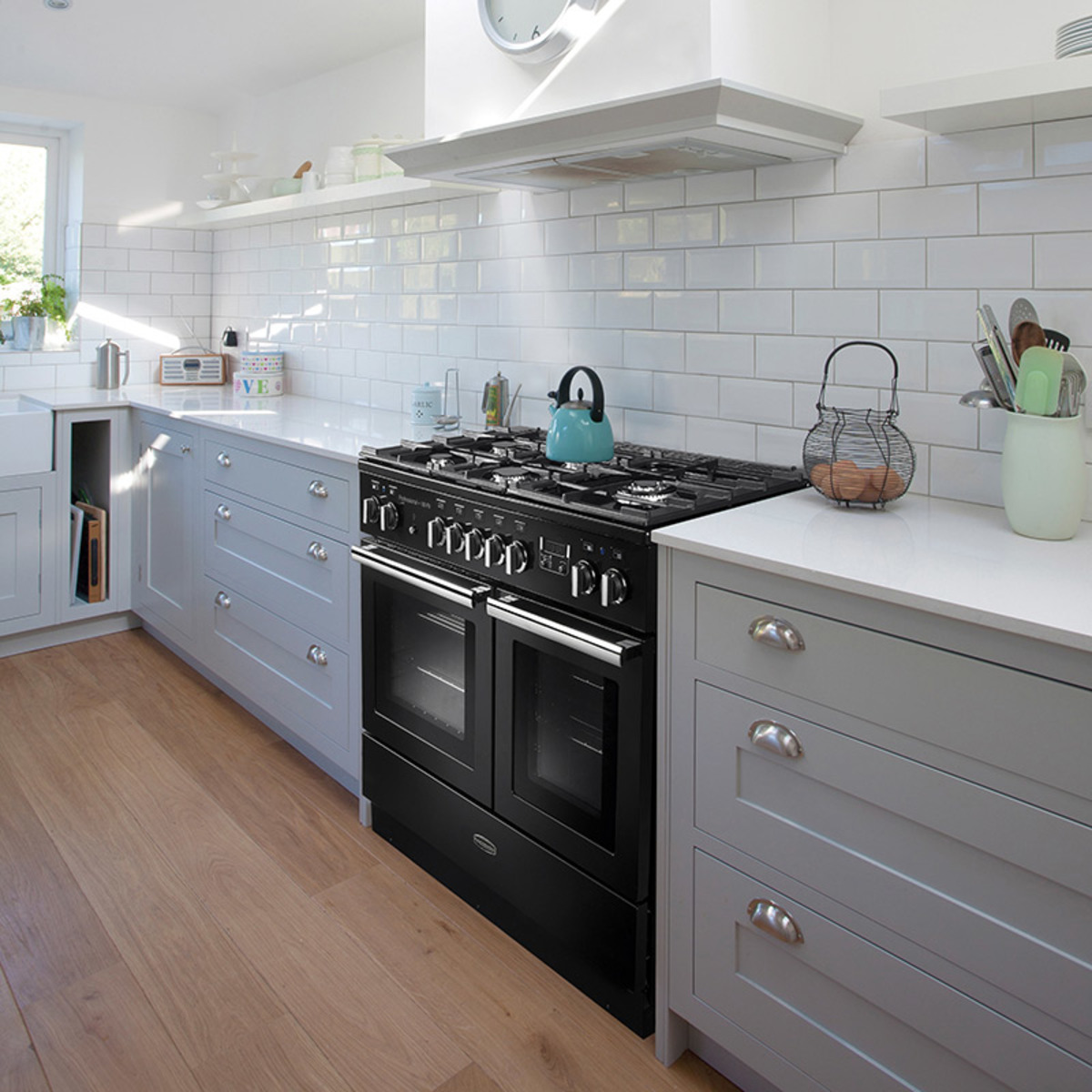 Black Rangemaster PROPL100FXDFFGBC Professional Plus FX dual fuel range cooker with two ovens, five gas burners, and a sleek design, set in a modern kitchen with light cabinetry.