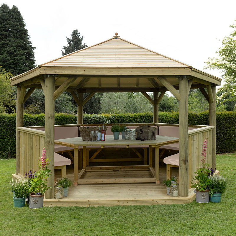 Luxury wooden gazebo with a timber roof, featuring a spacious seating area for up to 19 people, surrounded by planters with flowers, set in a green garden.