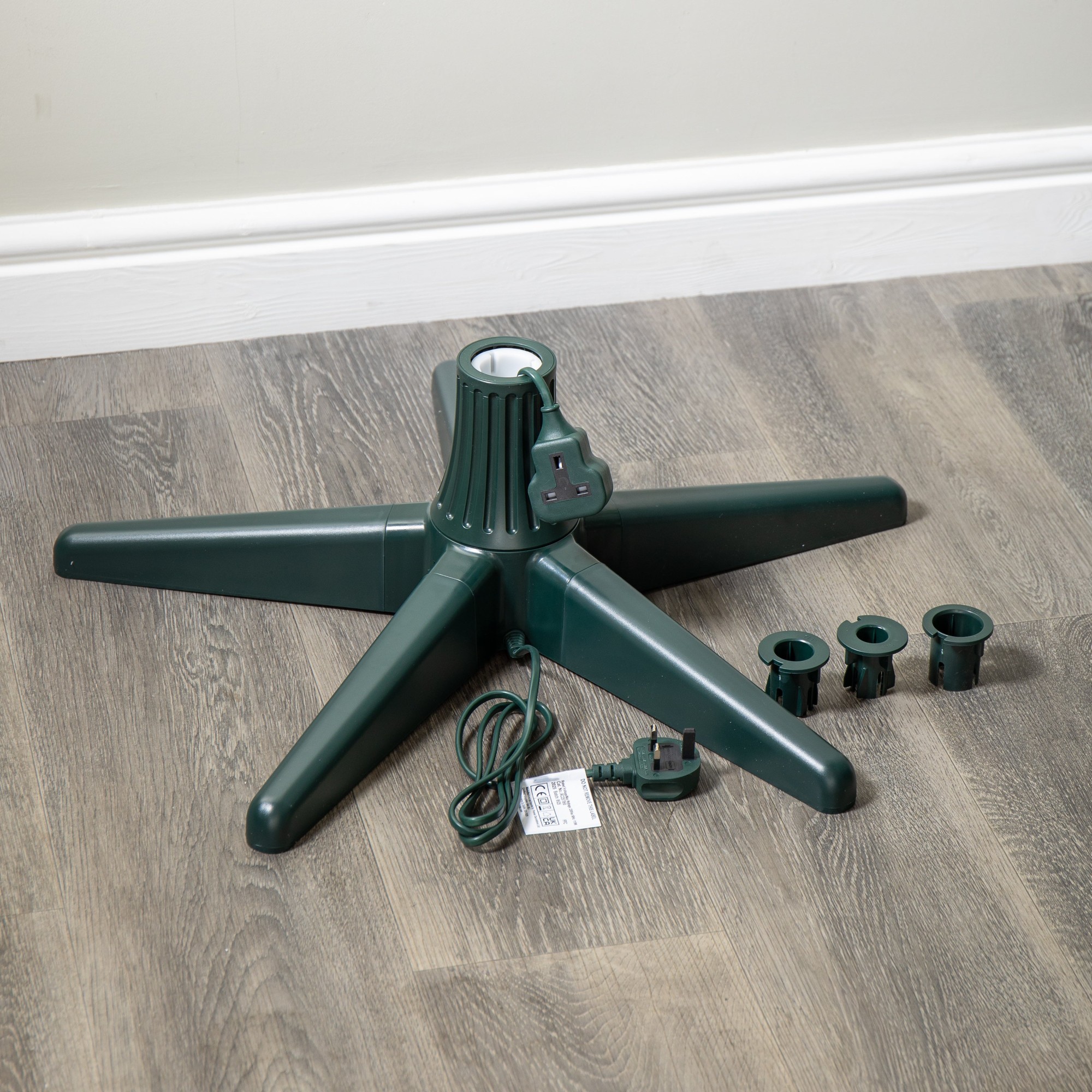Green plastic rotating Christmas tree stand with five sturdy legs, designed for trees up to 2.4m, includes three adjustable tree holder rings and a power cord.