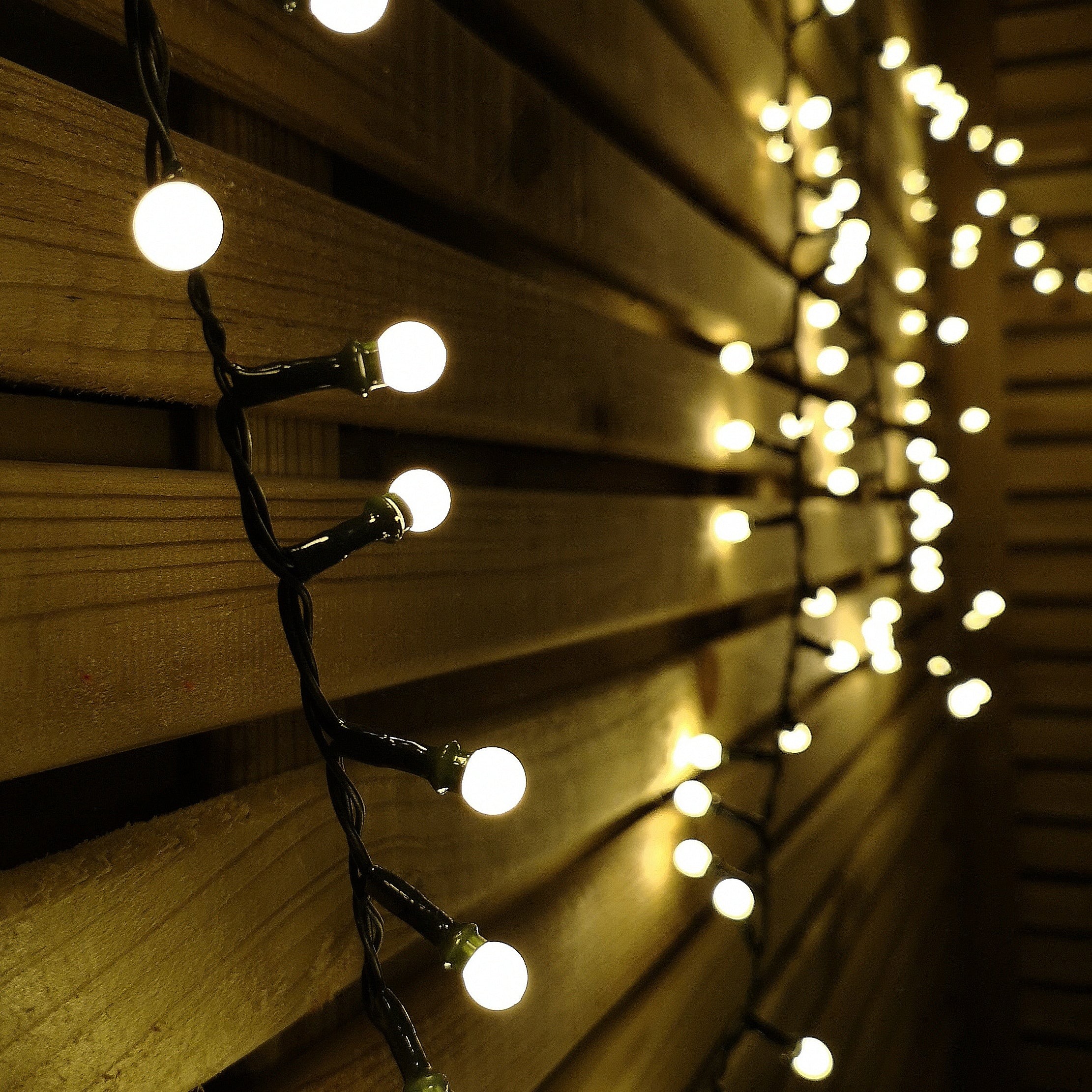 Warm white frosted berry Christmas lights with 150 LEDs on a black wire, draped against a wooden backdrop, creating a cozy, festive ambiance.