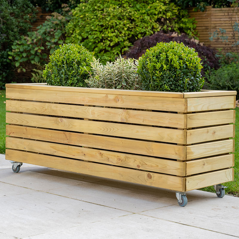 Wooden garden planter in natural finish, measuring 3'11" x 1'4", features horizontal slats, wheels for mobility, and is topped with lush green plants for a vibrant look.