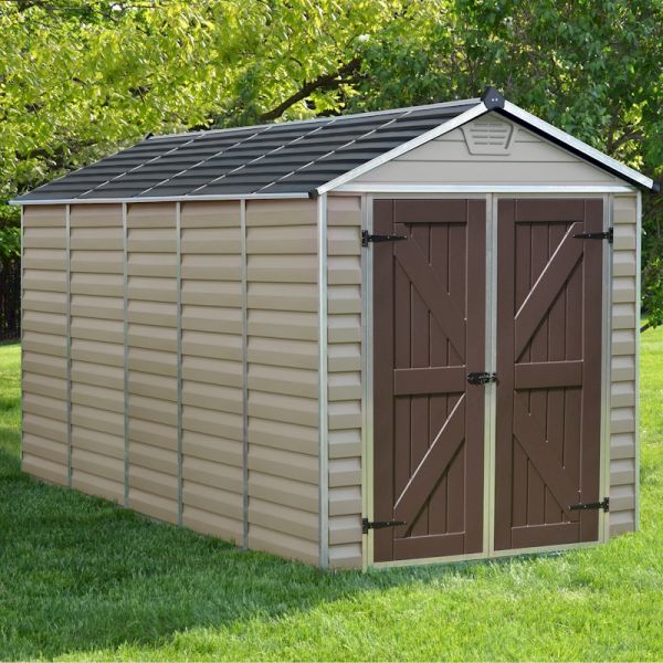 Tan plastic shed with a sloped black roof, double brown doors, and vertical siding, measuring 6' x 12', set on green grass with trees in the background.